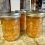Glass jars of golden ginger pear jam with fresh pears and ginger root on a rustic table
