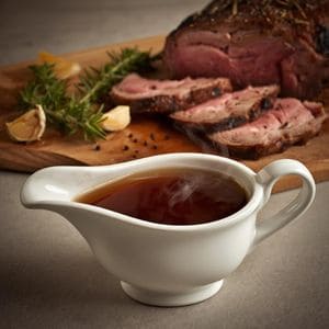 Thick slices of medium-rare prime rib on a platter with a small bowl of dark, savory au jus.