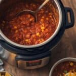 Bowl of hearty Instant Pot chili topped with shredded cheese and green onions, served with cornbread on a rustic table.