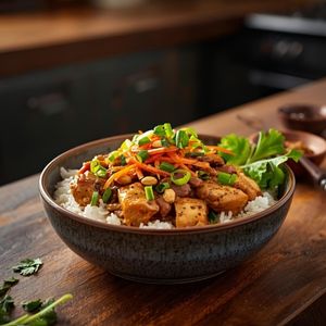 A bowl of sliced chicken breast drizzled with creamy peanut sauce, served over white rice with shredded carrots and fresh cilantro.