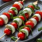 Caprese salad skewers with cherry tomatoes, mozzarella, basil, and balsamic glaze on a summer picnic table