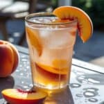 Glass of peach iced tea with fresh peach slices and mint leaves on a sunny summer table