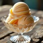 Close-up of vibrant peach sorbet scoops in a glass bowl with a spoon.
