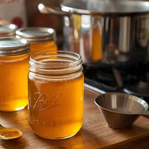 Jars of homemade apple jelly with fresh apples and canning supplies