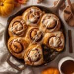 Pumpkin cinnamon rolls topped with creamy frosting on a white plate