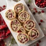 Cranberry pinwheel appetizers arranged on a white holiday platter with pine accents.