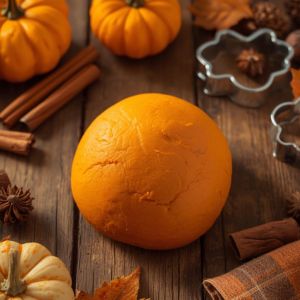 Soft orange pumpkin pie playdough with mini pumpkins, cookie cutters, and fall leaves on a rustic table.